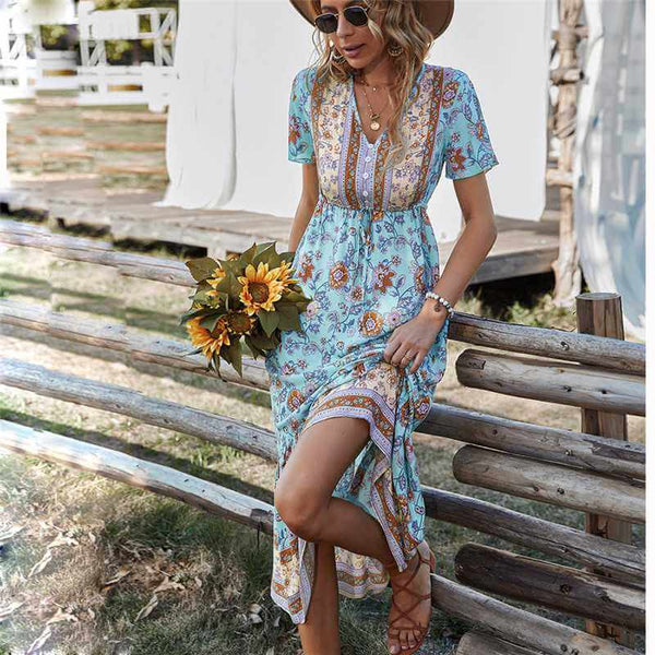 Woman in a floral Bohemian Midi Dress holding sunflowers, standing by a wooden fence in a sunny outdoor setting.